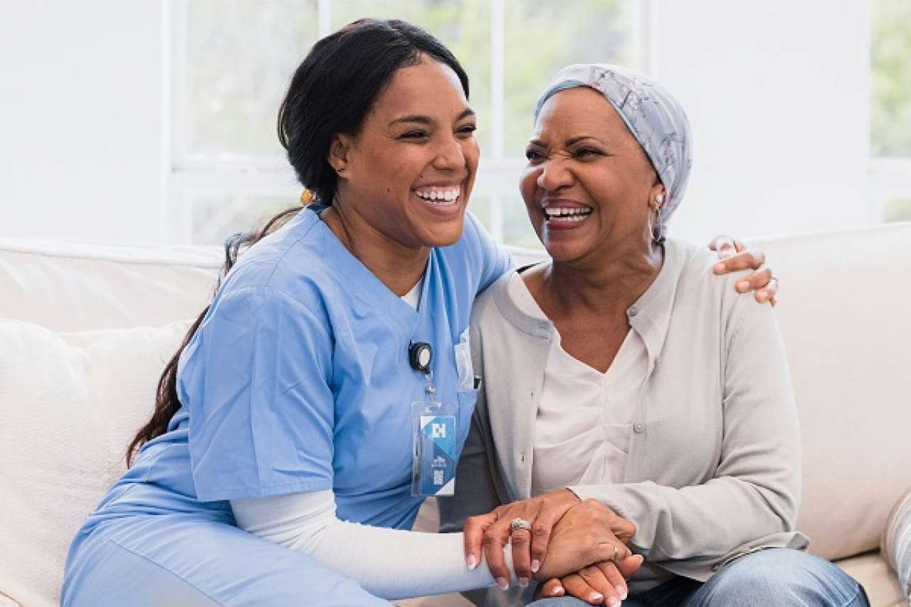 A smiling nurse sits next to a smiling patient.