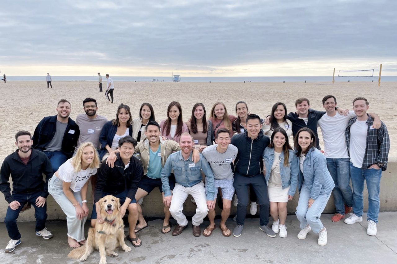 A group 21 anesthesiology residents pose for a photo on a beach with a dog.
