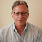 Person with face blurred wearing a light striped button-down shirt against beige wall