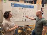 Rachel Fox is listening attentively to Matt Heffel as he gestures at a display board showing a Science Day project