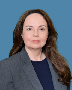 Tatjana Josin wearing a navy-blue shirt and grey blazer, with a neutral face looking at the camera in a professional setting. 