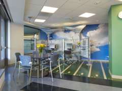 Teen room at child life. The floor resembles a football field, it has two computer work stations, and the wall has a blue sky full of clouds.