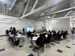 A group of people seated in a large room, attending a presentation with a projector screen.
