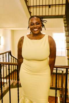 DGSOM student Tammara Davis stands in front of a staircase railing and wearing a yellow dress. 
