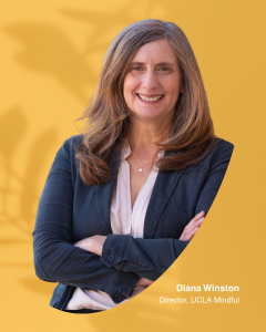 Head-and-shoulders portrait of a woman in a blazer with arms crossed on a yellow background
