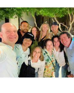Group photo of eight people smiling outdoors with trees in the background.