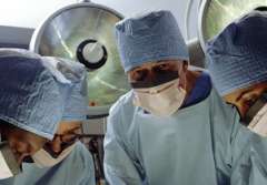 Four surgeons in scrubs and masks focused on a surgical procedure.