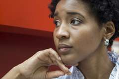 African American woman looking pensive, resting her chin on her hand against a red background.
