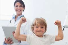 Small boy flexing at camera with doctor in lab coat standing behind him