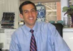 Dr. Gary Schiller in a light blue shirt and striped tie, seated at his desk.