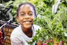 Child smiling next to leaf lettuce plant