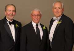 Three men in tuxedos with boutonnieres standing together.