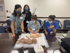 Medical team practicing neonatal resuscitation on infant manikin around a table.