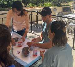 Four people painting terracotta pots at an outdoor table