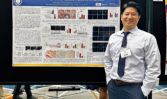 A man confidently stands next to a poster with hands on hips.