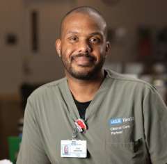 Chaz Valentine in a clinical care uniform, seated in a healthcare setting.