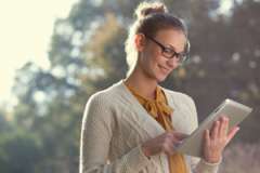 woman outdoors holding a tablet and smiling