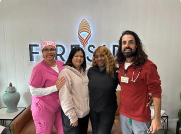 Four people standing by a wall logo; one in pink scrubs and one with a stethoscope.
