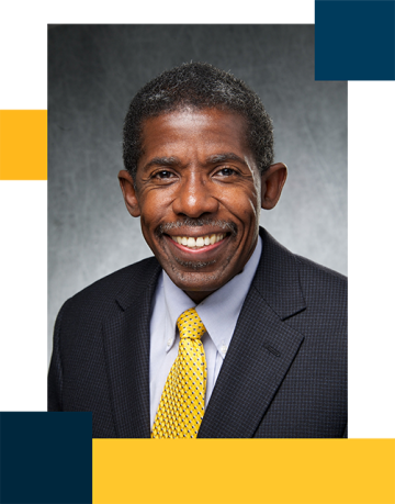 Dr. Dale Able wearing a black suit with white shirt and yellow tie