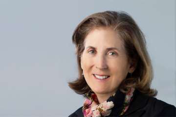 Dr. Judith Currier with brown hair, wearing a black jacket and a patterned scarf. Her direct gaze conveys confidence and approachability.