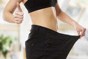 woman in large pants celebrating her weight loss and giving a thumbs up