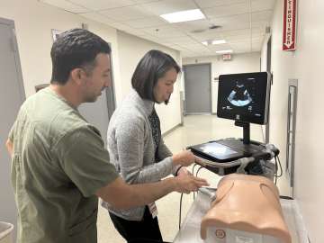 Two people using ultrasound probe on a medical manikin
