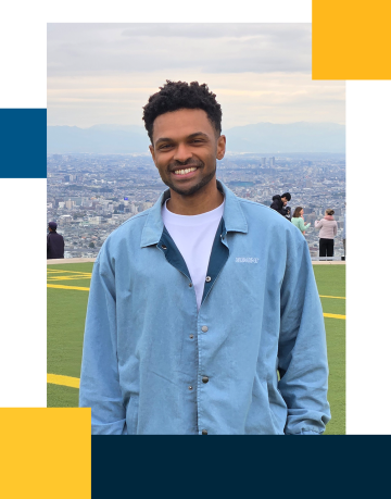 Jarrod is smiling with a light blue buttoned jacket with a city and mountainous landscape backgound