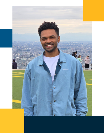 Jarrod is smiling with a light blue buttoned jacket with a city and mountainous landscape backgound