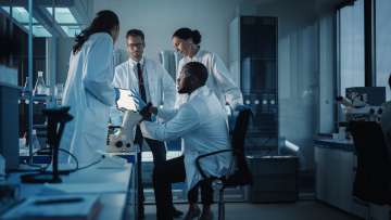 Group of researchers huddle together and collaborating in a lab