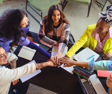 Diverse group of colleagues joining hands over a table during a team meeting