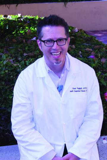 Smiling person in a white lab coat seated outdoors
