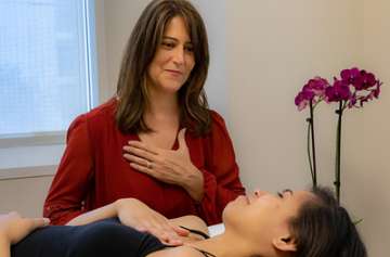 Woman sitting bedside with patient teaching them relaxation techniques