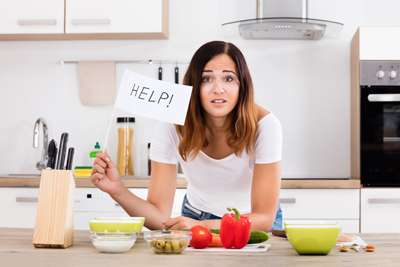 Woman in kitchen holding a sign that says, "HELP!"