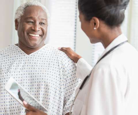 Doctor with digital tablet comforting older man in hospital