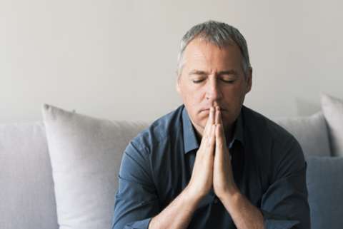 Man sitting with eyes closed on the couch with hands together 