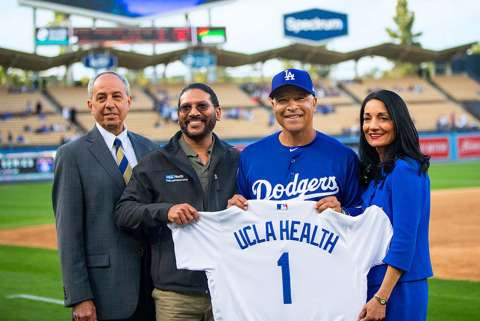 UCLA Health leaders and Dodgers coach holding a uniform with the writing that says UCLA Health 1.