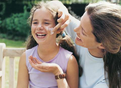 Woman putting lotion on girl's cheek