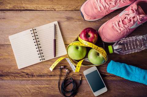 Running shoes, apples, a water bottle, notebook, and smartphone on a wooden surface.