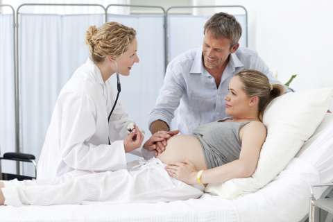 Doctor speaking to pregnant woman and her husband in hospital room