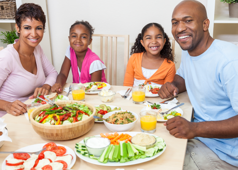 Smiling family enjoys a colorful, healthy meal together at home, promoting balanced nutrition and wellness through shared meals.