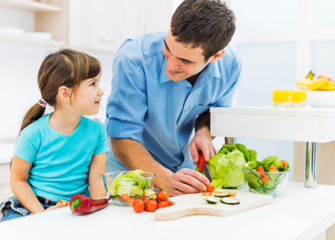 A father and his daughter cutting vegetables in the kitchen while prepping a meal.
