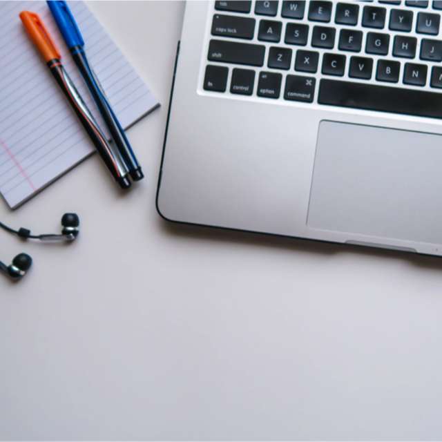 a laptop, notepad, and 2 colored pens on a desk