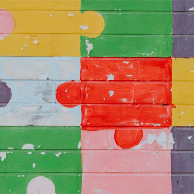 brick wall with puzzle pieces of different colors painted on it.