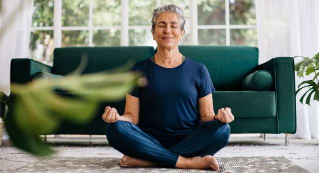 Senior woman meditating in lotus position at home.