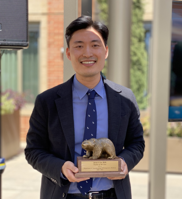 Dr. Jason Lee smiling while holding a UCLA award plaque shaped like a bear, presented by the Department of Anesthesiology.