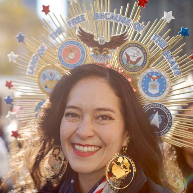 Smiling woman wearing ornate sunburst headpiece adorned with U.S. military seals