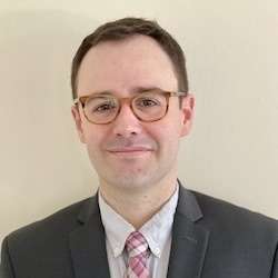 A smiling man with glasses and a grey suit.