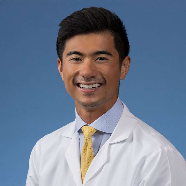 Dr. Kekoa Taparra posing, wearing a white coat and smiling.
