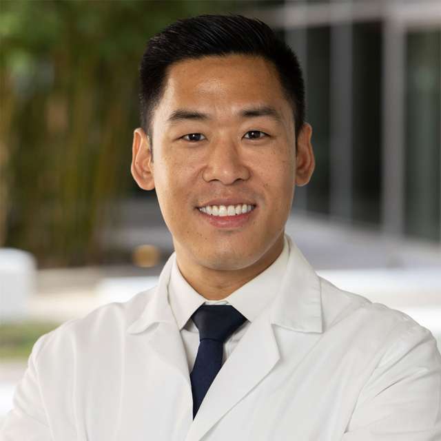 Dr. Alan Lee posing outside, wearing a white coat and smiling.