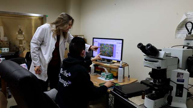 Two people in a lab, one in a white coat pointing at images on a computer monitor